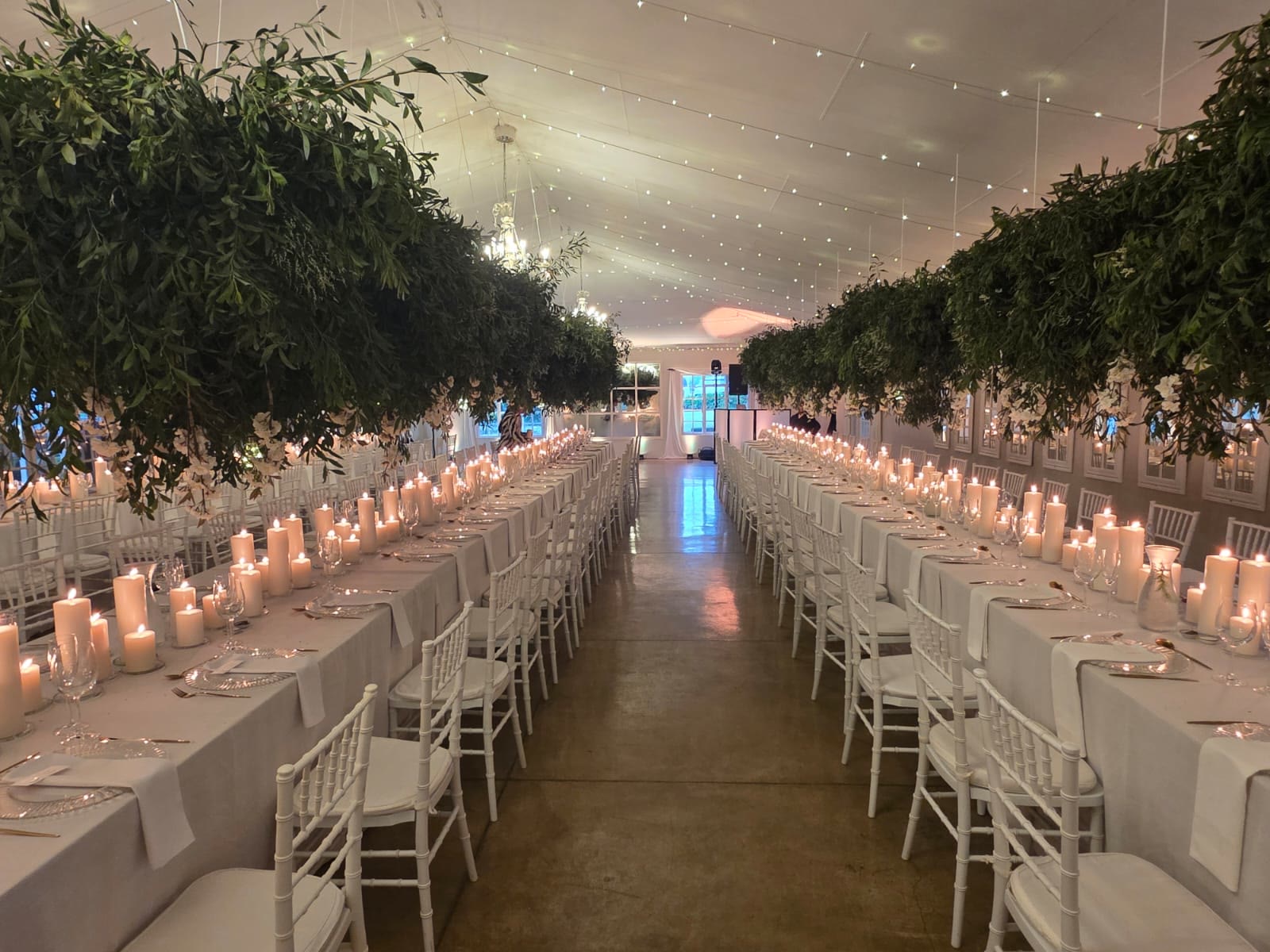 Stunning long banquet table setup at Providence with lush greenery canopy overhead, hundreds of pillar candles lining tables creating candlelit pathway, white linens, fairy lights, chandeliers, natural romantic wedding decor at KZN Midlands venue