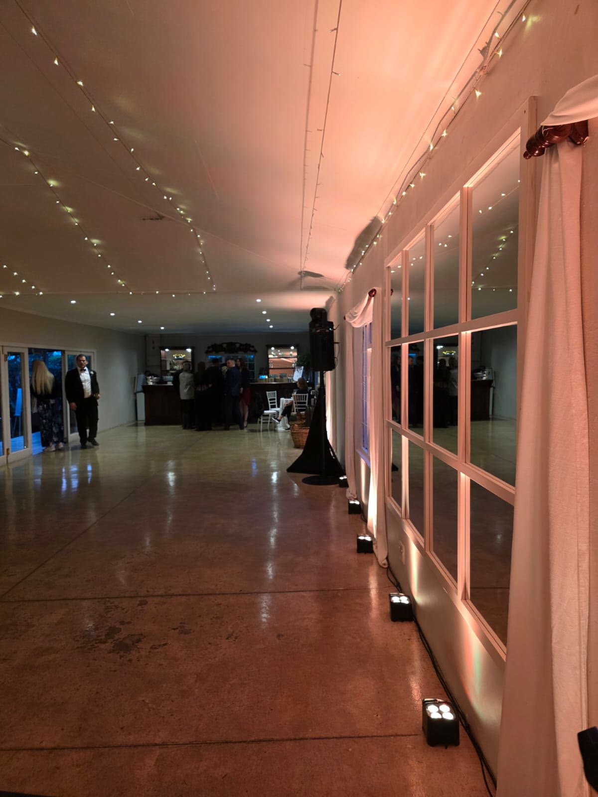 Providence venue entrance hallway with elegant pink uplighting illuminating white French door windows floor to ceiling, polished reflective floors, white drapes, fairy lights on ceiling, guests visible in background at Nottingham Road wedding