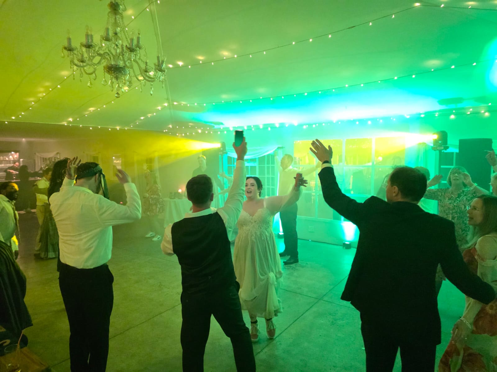 Bride dancing with wedding guests at Providence Country Weddings with vibrant green and yellow uplighting effects, crystal chandeliers, fairy lights, and atmospheric smoke creating energetic celebration atmosphere in KZN Midlands venue