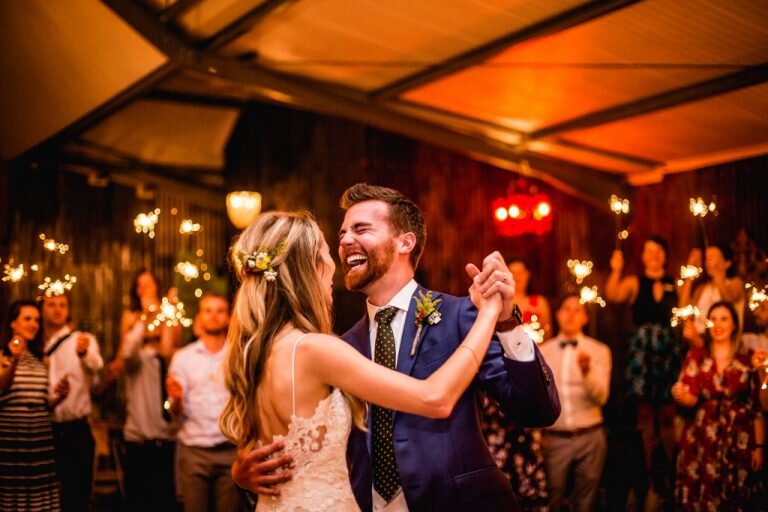 Wedding guests celebrating on a packed dance floor with hands raised during reception party